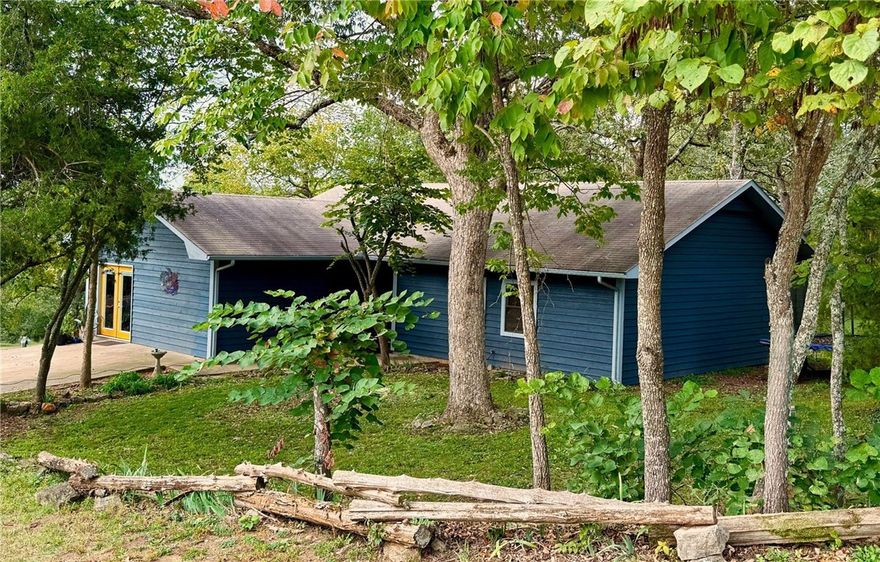 Walk down to the river for world-class trout fishing or launch a canoe for an afternoon float from this  wonderful White River Estates property. The 3BR/2BA home features an open floor plan that's perfect for family gatherings. The living room boasts beautiful wood floors and a wood-burning fireplace. The updated kitchen has custom cabinets, granite counters, and stainless steel appliances. Double doors in the dining area open onto a large covered deck, making outdoor entertaining easy. A spacious ensuite bedroom, two guest bedrooms, and a full bath complete the floor plan. A wet-weather creek with a stone creek bed runs along the west side of the property to the river. A 12' x 20' storage building could serve as a workshop. There's additional storage in the attic and under the deck. You'll enjoy the fenced garden area surrounded by a variety of fruit trees. A new Generac generator comes with the property. The exterior of the home has a fresh coat of paint. Just minutes to Beaver Lake and downtown Eureka Springs.