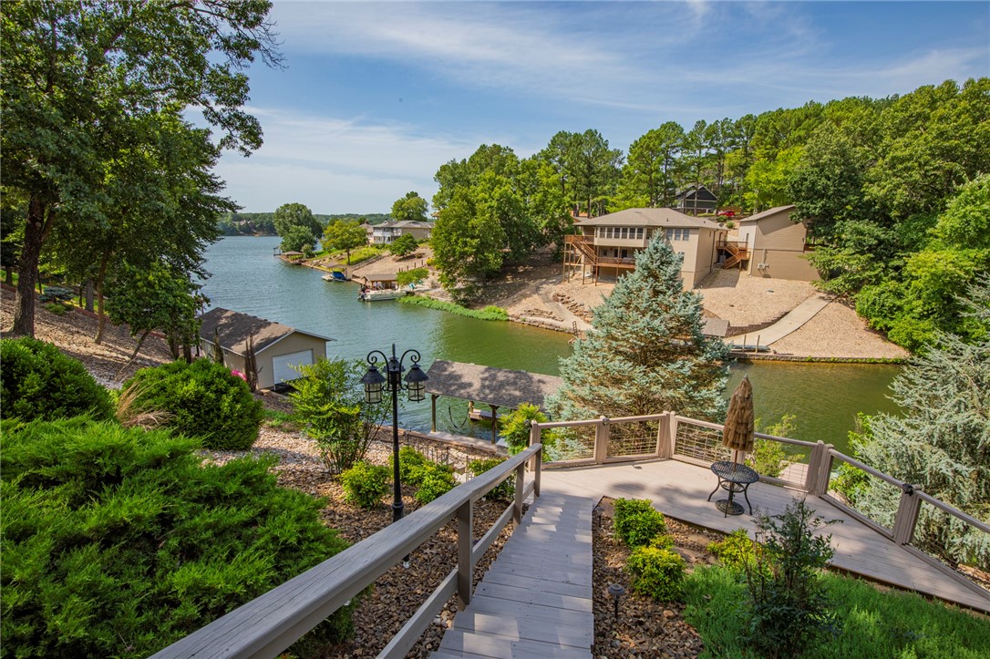 Enjoy LAKEFRONT living at its best on beautiful Lake Loch Lomond - Bella Vista's largest lake! Listen to the WATERFALL feature as you comfortably enjoy the day on the expansive DECK at the COVERED DOCK with great fishing from the dock, water skiing, swimming, floating in the private cove OR take a lake ride to Lakepoint for dinner! Just minutes from I49 to drive to Bentonville too! This fantastic home has 4 BRs + an office/guest room with Murphy bed, SUNROOM, & more! OPEN floorplan with vaulted ceiling, Oak hardwood floors & lovely VIEW! Kitchen features a breakfast area, roll out drawers and stainless steel appliances. Downstairs large Family room has a wet bar, full bathroom, and STORAGE that can be an exercise room or workshop! MANY UPDATES include a new roof in 2020. Also this Home has a GENERATOR! The THREE car garage is a real bonus with lots of room! GORGEOUS professional landscaping, multiple decks & COVERED lower deck. Yard has a nicely fenced area if needed. 3 BR septic & Select HOME WARRANTY included!