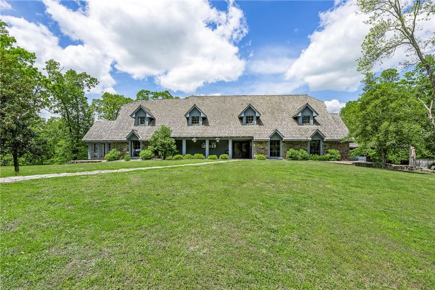 Welcome to this gorgeous, 1974 architect-built estate, situated on over 20(+/-) acres in NE Rogers. This private gated home is just minutes away from Downtown. As you enter the tree lined driveway, you are greeted by fields & your very own waterfall close to the entrance. Entering the home, you are welcomed by a great room w/ 16ft cathedral ceiling, German schmear floor to ceiling stone, wood burning fireplace, & beautiful chandeliers. Off the entry, a formal sitting area/study leads you to the primary bedroom. This spacious grand-suite boasts its own sitting area that opens to the courtyard/pool. Main level additional living spaces give privacy to guests or could make a great mother-in-law suite w/ a sunroom. Custom built-ins & high-end appliances can be found in the eat-in-kitchen & butler’s pantry. The grounds are an ideal retreat filled w/ lush landscaping, courtyard, gazebo, in-ground pool, tennis court, greenhouse, garden & lots of open space to entertain. Newer paint, light fixtures, & carpet.
