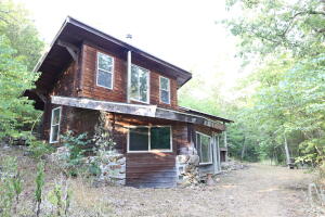 Take a short drive into a valley and be transported into the most peaceful and private location you can imagine. Nestled at the base of the mountain, set where two year-round spring fed creeks meet, you will find the most whimsical cottage that is 100% off grid. A small waterfall flows into the creek, providing ample water that flows into a 750-gallon holding tank. A reverse osmosis system creates clean drinking water for the home. A solar panel is set on the hillside and provides enough power to run the pump and electric in the home. There is a wood burning stove centrally located, but heat can also be provided by propane wall heaters. The home is full of hidden artistic details and uses natural elements for structure, including the rock staircase leading to the second level. Kitchen has