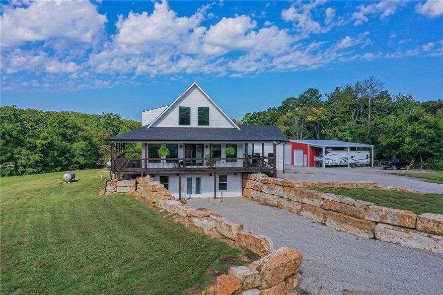 Built in 2023 and nestled on 15 acres, this three-story 4174 sq ft house with 1328 sq ft of wrap around porch offers it all. The main level features an open plan great room with cathedral ceilings, a fireplace, and a stunning staircase. The gourmet kitchen features granite countertops and upgraded appliances (refrigerator conveys).  The primary bedroom opens to the porch with serene country views and a seasonal spring. The primary bathroom has an enormous, tiled shower and his and her closets. A half bath and mudroom complete the main level. The upstairs offers two bedrooms, a full bath, and extra storage. The walk-out basement includes a huge family/game room, office, two bedrooms and a FEMA approved saferoom. A generator and outdoor wood furnace keep this home comfortable and functional even during storms. In addition to the dream home, the property includes an 1800 sq ft heated/cooled shop (2808 under roof) with kitchen, bathroom, and septic system making this a perfect opportunity for an Airbnb or venue.