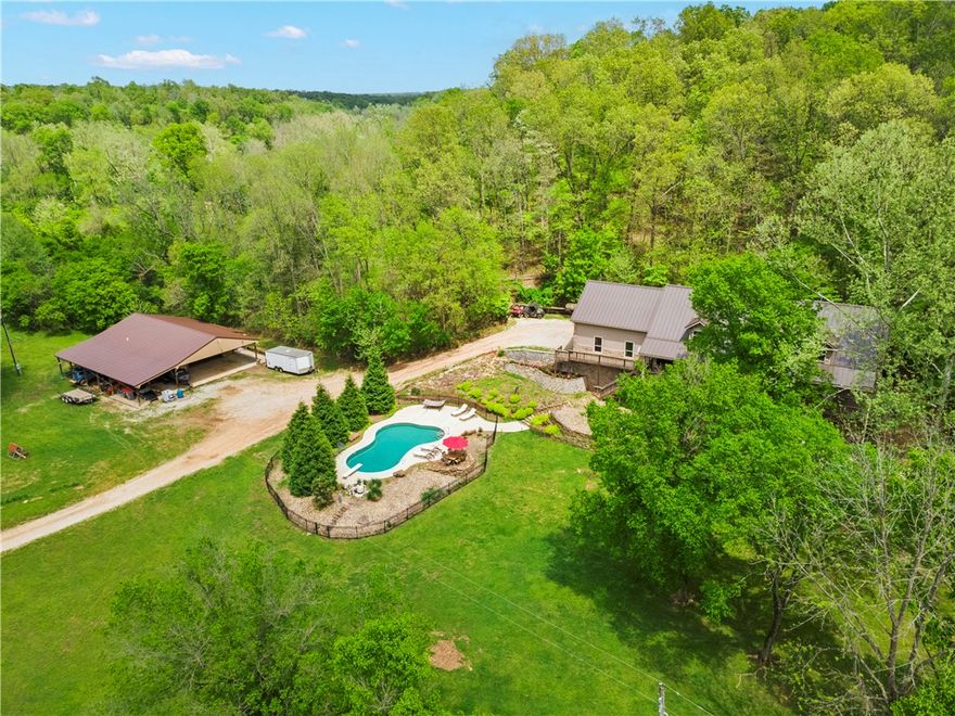 Welcome home to this incredible estate on almost 30 acres of treelined countryside with no visible neighbors. This stunning 6 bedroom, 5 bath home features 3 levels with extra large bedrooms, 500 sf bunk room with separate entrance, and wrap-around porch with fans.
The kitchen showcases custom cabinets with soft close drawers and high-end appliances including a 48" GE Monogram range. The master suite offers 2 separate closets, custom vanities, and a heated shower with Bluetooth speaker.

The basement includes a theater room, handmade Walnut bar top, and second laundry. The home features central vac, laundry chute, whole house spring water filtration, and a high efficiency Ashley wood stove.
The 50x50 shop includes a heated/cooled office, RV hookup, and walk-in cooler. Outdoor amenities:  private acreage, low chlorine pool, fenced pasture, natural springs, 1/2 mile walking trail, and gated entrance. New metal roof (2022).

Property is not in a FEMA designated flood zone and does not require flood insurance