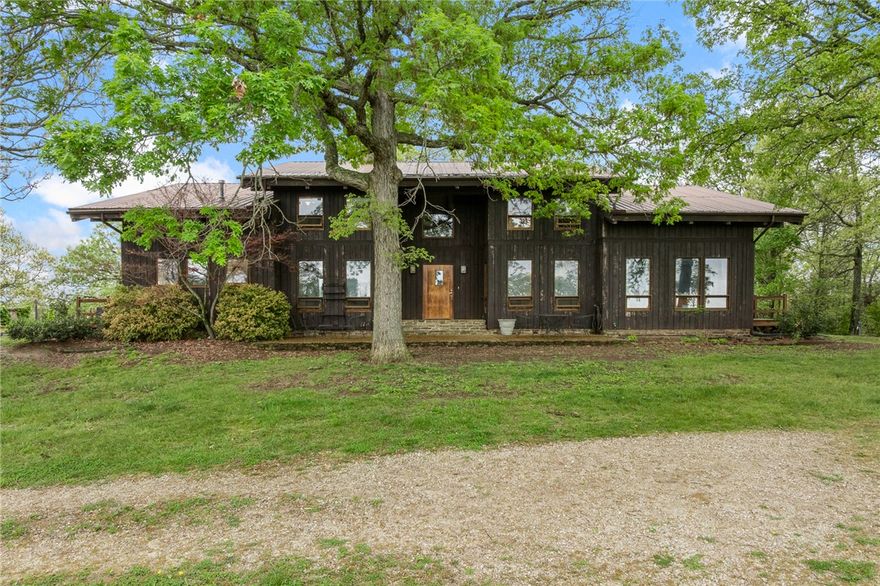 Tucked into the breathtaking Boston Mountains near Huntsville and Osage, this rare Ozark retreat offers unmatched privacy, character, and natural beauty. The stunning 6,434 sq ft contemporary home features 4 bedrooms, 4.5 baths, soaring 26’ ceilings, rich oak and walnut finishes milled from the property, and a dramatic two-story fieldstone fireplace. A finished walk-out basement with workshop connects through a one-of-a-kind stone tunnel to a 3-car garage. A charming 544 sq ft guest cabin with loft, full kitchen, spacious porches, and 2-car carport provides ideal guest or rental space. The 32x50 barn includes electric, 3 stalls, tack room, and pens. The land showcases rolling pasture and timber, fenced and cross-fenced, with 3 ponds, a natural spring, trails, vineyard, and garden space. Shared deep well, mineral rights
convey. Just 15 miles to the Buffalo National River—perfect for a private estate, recreation, or investment opportunity.