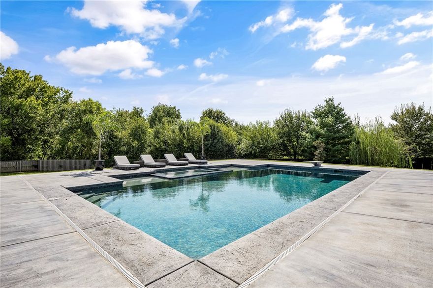 Discover unmatched luxury in this 7,600+ sq ft modern masterpiece in Bentonville’s prestigious St. Valery’s Down. A striking stucco-and-stone exterior with standing seam metal roof sets the tone. Step inside to soaring two-story spaces, a dramatic living room with a horizontal fireplace wrapped in shou sugi ban wood and metal, and walls of glass opening to the resort-style patio. The chef’s kitchen boasts an oversized island, Wolf 8-burner gas cooktop, and built-in refrigeration. Entertain in the pool room with full bar, pool table, and surround sound, or retreat to the theater. Outdoors, a heated saltwater pool with tanning ledge and infinity spa delivers a private resort experience. Every bedroom offers an ensuite bath, while whole-home audio, app-based automation, and tongue-and-groove porch ceilings elevate daily living. Sophisticated, bold, and designed for both grand entertaining and intimate relaxation—this estate is Bentonville living at its finest.