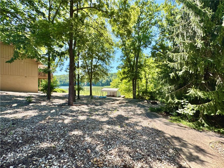 Lake living at its finest on Lake Loch Lomond! Welcome home to 3BD/3BA property with office & downstairs bonus room offers an easy, level entry & a gentle walk to the water. Enjoy your own covered boat dock & a low-maintenance rock yard. The vaulted ceilings and open layout connect the living, dining, and kitchen areas — complete with granite counters, custom island and extra storage and bar seating.  Take in serene lake views from the 4-season enclosed porch or the spacious back deck overlooking the level yard. The walk-out basement includes a 3rd bedroom and bonus space or a second family room. Updated primary suite features a walk-in shower, whirlpool tub & dual vanities. 3-car garage, walk-through laundry access to the kitchen on primary floor. Whether boating, relaxing or entertaining, this lakeside retreat has it all! Back deck pressure washed & stained, pressure washed front drive & back sidewalk to dock. Property has had recent updates to the home! Must see to appreciate level lot in Bella Vista!