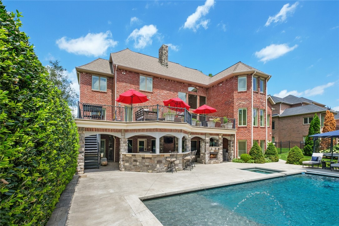 Located in a gated luxury neighborhood, this stately three-level home is a masterpiece of brick and stone. Inside, the grand living room features a two-story ceiling, a beautiful fireplace with a dark wood surround, and a balcony overlooking the space. The gourmet kitchen is a chef's dream with white cabinetry, a large center island with seating, a professional-grade range, and elegant gold light fixtures. This home offers 6 bedrooms, 6 bathrooms, and 2 half bathrooms, with all bedrooms featuring en suite baths. The primary bedroom is a serene retreat with a spa-like bathroom boasting a soaking tub, a large walk-in shower, double vanities, and marble. For entertainment, the home offers multiple game rooms and a dedicated media room. The backyard is an entertainer's paradise with a luxurious swimming pool, a large patio, and a covered outdoor living area with a stone fireplace and a built-in bar. The home is conveniently located close to shopping, I-49, the Walmart AMP, and local trails.
