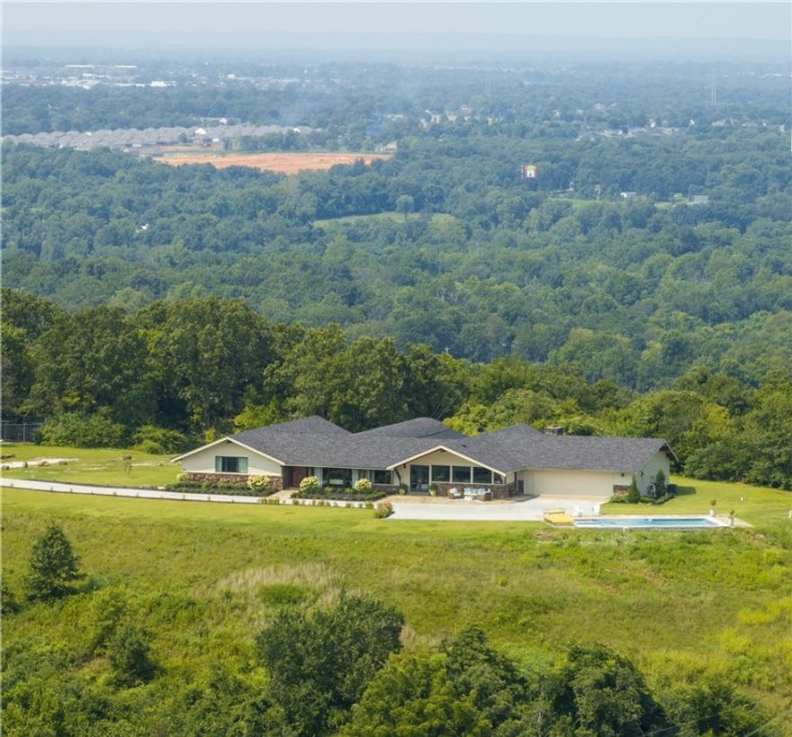 5+acres 1970’s mid-century modern prairie style 1 story estate home, totally remodeled, new roof, pool, HVAC, plumbing. 7878 living SF; (6571 H/C SF) a 36’ long screened in porch, 11x22 coved flagstone patio off the mother-in-law suite and a front 700 sf flagstone covered patio with the best view around! 5 large bedrooms, 4 full and one half baths. Flagstone, oak wood & heated marble floors. Wood, beamed, vaulted tongue and groove ceilings with redwood beams made in Washington state and shipped by train to Springdale. Sunken conversation pit in front of the fireplace with 14’ cedar mantle. Custom Built-ins. Soft close drawers, brass hardware, wood pocket doors, custom 46” walnut front door. Lots of storage. Butler’s pantry with 2nd fridge, warming drawer and sonic ice machine. Heated pool with hot tub and auto closing cover. This is a quality, trophy property with a north facing view and on a clear day, you can see Madison & Carrol County to the east and Centerton to the west. Freshly paved private, gated driveway.