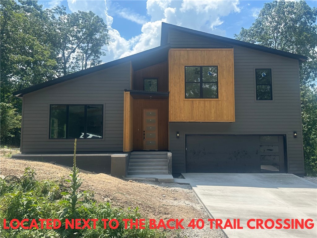 Discover this stunning modern new construction on a large .32-acre wooded lot with serene views. Located next to the Back 40 Trail Crossing and just moments from Lake Rayburn, Metfield Golf Course, and Downtown Bentonville. This home offers both convenience and tranquility within the Bentonville School District. Features include an open floor plan showcasing elegant beams and beautiful custom cabinets. The kitchen is equipped with 3 cm quartz countertops and premium stainless steel appliances, including a gas range. Enjoy the spacious primary bath with a large custom walk-in tile shower. High-end finishes throughout. No carpet for easy maintenance. Complete with an oversized outdoor patio, this home is perfect for entertaining or simply relaxing in nature.