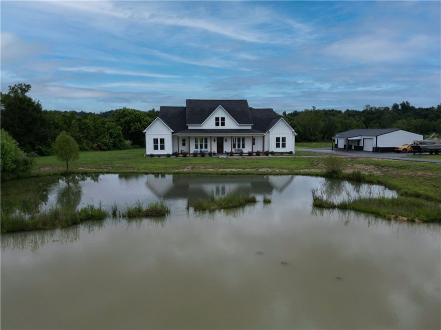 Experience refined country living just minutes from town in this gorgeous 4 bed, 4 bath custom home on 5 private acres. Built in 2022, this 3,160 square foot home features soaring beamed ceilings, 8’ doors, and sunlit rooms with views in every direction. The kitchen has a quartz island with seating, quartz countertops and ample storage space plus there is an extra large separate pantry. Laundry room is located off the primary suite for convenience.   A spacious bonus room with a full bath is over the 3-car garage—perfect for home theater or rec room. The crown jewel? A massive 600 square foot covered back patio designed for entertainment and enjoyment. Whether hosting friends or soaking in the quiet, wooded surroundings and flowing creek beyond, this is your private retreat. A spring-fed, stocked pond sits in front, and a 1,500 sq ft metal shop completes the package.  We invite you to come and enjoy the quiet of the Valley.