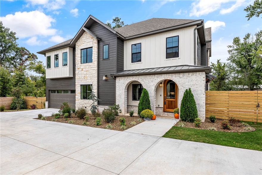 This residence blends refined style with modern comfort, featuring a soft color palette, brushed gold accents, designer lighting, and matte-finished white oak floors. The living area centers around a cozy fireplace flanked by custom glass-paneled cabinetry. The main-level primary suite offers a paneled feature wall and a spa-inspired bath with onyx pendant lights, marble-veined tile, dual shower heads (including rain head), and seamless glass. Upstairs includes a large family room, two bedrooms with a Jack & Jill bath, a secondary suite, and a flexible fifth bedroom or office. Outdoor living is elevated with a covered front porch, open patio, grilling terrace, and a fully fenced, landscaped yard. Discover timeless luxury just moments from the best of Bentonville.