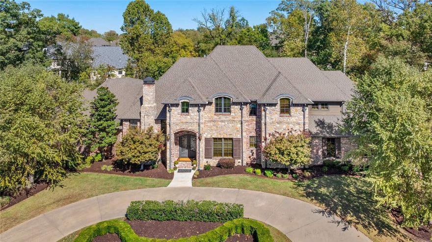 Resort style 5,540 sq ft estate in Pinnacle Country Club on a private 0.78-acre cul-de-sac in Bentonville School District. This fully updated home features natural stone & reclaimed brick exteriors, 5 en-suite bedrooms, 5 full & 2 half baths. Enter through French doors to a stunning foyer with round staircase, executive office, & formal dining. The open-concept layout connects the gourmet kitchen with top-tier appliances, custom rich cabinetry & large island to spacious living & dining areas with vaulted ceilings, exposed wooden beams & stone fireplace. Main level features 2 bedrooms, including a primary suite with private pool access & spa-like bath with dual walk-in closets. Upstairs: 3 bedrooms, theater/game room with savant controls & additional office. The backyard boasts a heated Gunite pool, swim-up bar, spillover spa, fireplace & outdoor kitchen. Additional features: 4-car+golf cart garage, updated multi-room Sonos sound system, wine room, wet bar, central vac, whole-house water filtration & storm shelter.