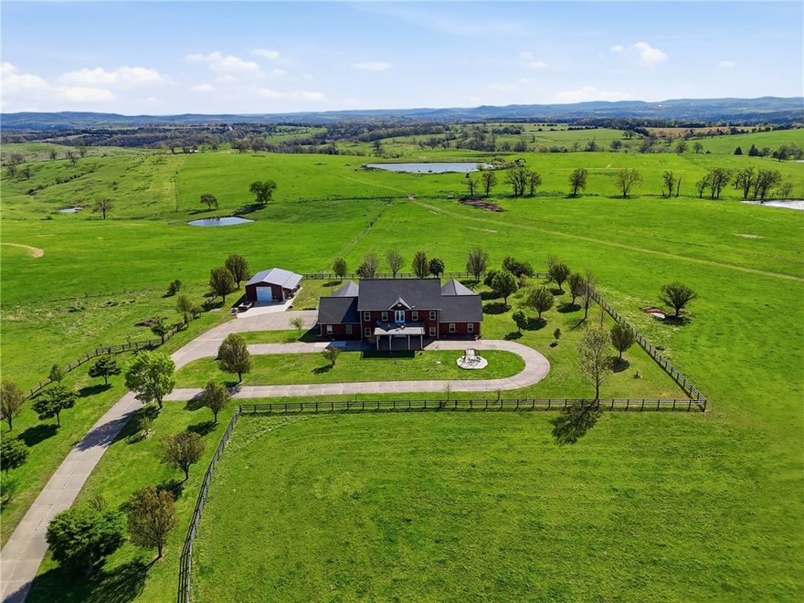 Beyond a private gated entrance, discover an elegant colonial-style estate set on 40 picturesque acres between two mountain ranges, offering sweeping views and open skies. Rolling pasture, a pond, and 6" steel fencing frame the property, with water faucets placed every 100 ft for convenience. The 6,032 sq ft brick home delivers refined living with 4 bedrooms and 4 full, 1 half bath—each bedroom featuring its own ensuite and walk-in closet. The main-level primary suite, ideal as an in-law suite, offers a private retreat with kitchenette, jetted tub, and spacious his-and-hers closets. Inside, 10-ft ceilings with coffered details enhance the formal spaces, complemented by hickory floors with black walnut inlay and granite countertops throughout. Enjoy multiple entertaining areas, including a sunroom with 8 person hot tub and an upstairs game room. A hidden concrete safe room with steel door sits behind a bookshelf. Complete with an oversized 3-car garage, 32x40 workshop with half bath, and 50-amp RV hookup.