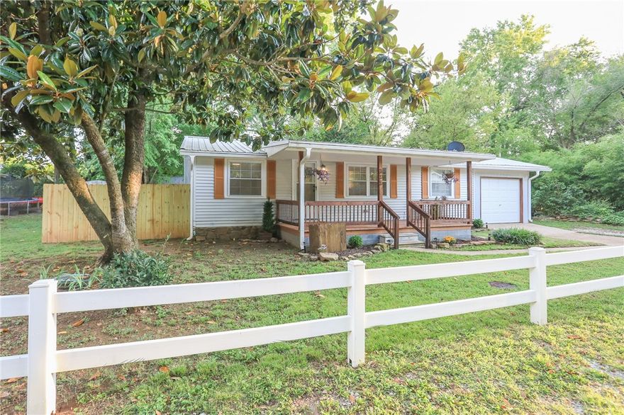 Step inside to discover beautiful pine hardwood floors and a spacious living room that flows into the dining area and kitchen, while the split floor plan provides privacy for the primary suite. Throughout the home you’ll find cordless faux wood blinds, custom cedar closets and updates including a new garbage disposal (2025). Kitchen appliances, washer, and dryer convey with an acceptable offer! Enjoy the outdoors in the fully fenced backyard with a brand-new fence. A Lily Magnolia blooms twice a year with stunning purple flowers, complemented by mature Magnolia trees in the front and back. The large covered front deck is the ideal spot for morning coffee or evening relaxation. Located in a quiet neighborhood within walking distance to downtown, schools, parks, library and the new splash pad, this home combines small-town charm with unbeatable value. Don’t miss your chance—homes this clean and this cute at this price point in NWA are rare!