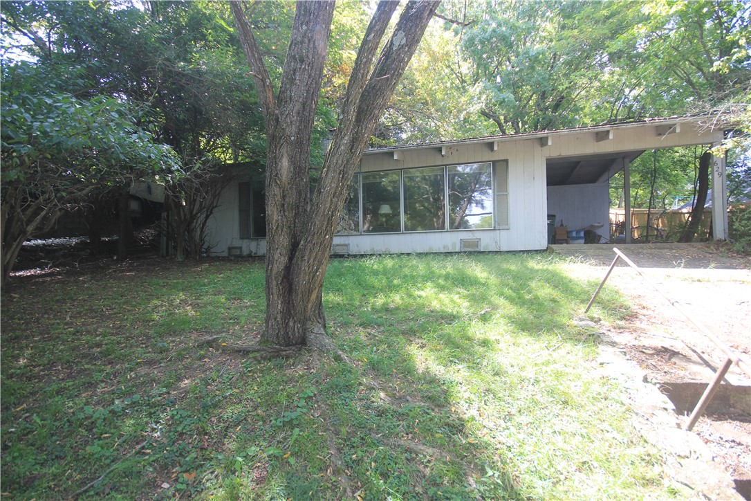 This 2-bedroom, 1 bath home offers character and charm with its painted wood-beam ceilings, hardwood flooring, and a stunning white brick fireplace accented by a mirrored wall. Large picture windows flood the living room with natural light, while built-in shelving add both storage and style. The kitchen features an island with a built-in cooktop, an eat-in dining space, and access to a spacious enclosed covered patio. Situated in an area of established homes and just minutes from historic downtown Fayetteville and the University of Arkansas, this property is a rare find. While it does need significant updates and repairs, it holds great potential to become a beautiful home or investment.