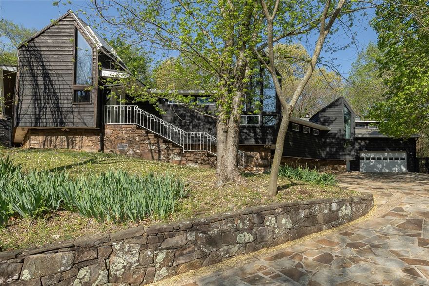 Designed by a renowned architect, this incredible Fayetteville home is rich with character & history. Tucked off Mission Blvd on 0.62 acres, it features stonework by Fay Jones' mason, flagstone drive, stone walkways & walls, mature trees, & lush landscaping. Redwood siding wraps the exterior, while inside an open floor plan showcases 2 see-through fireplaces, 2x6 walls, oak hardwoods & LVP, plus wood ceilings throughout. The primary suite offers a fireplace, double vanity, walk-in shower, & jacuzzi tub. Enjoy a 1500 SF pressure-treated deck overlooking a heated saltwater pool (new pump 2022). Updates include newer metal roof (2010), heat pump (2019), windows, patio doors, & skylights. The kitchen features stainless appliances, with the refrigerator, washer, & dryer all conveying. A built-in bar area, pool table, & negotiable furnishings complete this one-of-a-kind property!