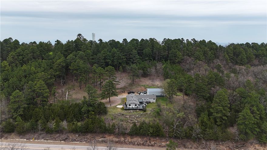 The three-bedroom, two-bathroom home presents an impressive aesthetic. It features Luxury Vinyl Plank (LVP) flooring, Knotty Pine tongue-and-groove paneling adorning the walls and ceilings, custom countertops, and a cedar kitchen bar. The kitchen is further enhanced by custom-built knotty pine cabinetry, a hammered brass farmhouse sink, and built-in appliances that are less than one year old.The composite deck extends across the southern and eastern elevations, ensuring years of minimal upkeep. Whether one is enjoying morning coffee while observing the sunrise over Mount Magazine or viewing the sunset from the comfort of the hot tub, the vista is truly unparalleled. Adjacent to the main structure is a 30x40 shop. The shop is insulated and equipped with a mini-split system, providing year-round climate control for various projects. Furthermore, the shop is plumbed for a future bathroom installation as well as a 9,000lb two-post car lift. .