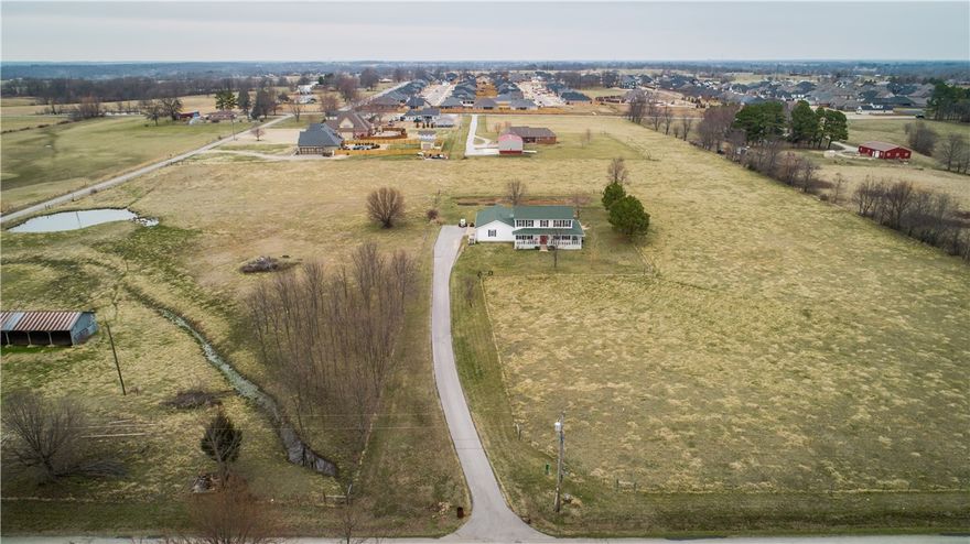 10.76 acres of development land with a farmhouse on the property. Acreage has tons of potential to be residential lots or could stay a country estate. Convenient location is minutes from 412W & Barrington Rd, plus 1.5 miles from HWY 112 for easy access to all of NWA. In addition, acreage is in an area with both new construction communities & individual estate homes. Water, electric, gas & septic are on the property. Sewer is approximately 210 ft East of property line on South side of Sbanotto Ave. The 10.76 acres are mostly level & open, in a square shape, and there is a pond & two outbuildings. Home has wrap-around porch on 3 sides & downstairs living space with foyer, living room, family room, eat-in kitchen, office, powder bath, mudroom/utility, bathroom with walk-in shower & 3-car garage. Upstairs has master bedroom with full bathroom, three guest bedrooms & guest full bath. Part of the property is zoned agriculture & part is zoned R-3, and it sits on a corner with frontage on both Sbanotto Ave & Ardemagni Rd.