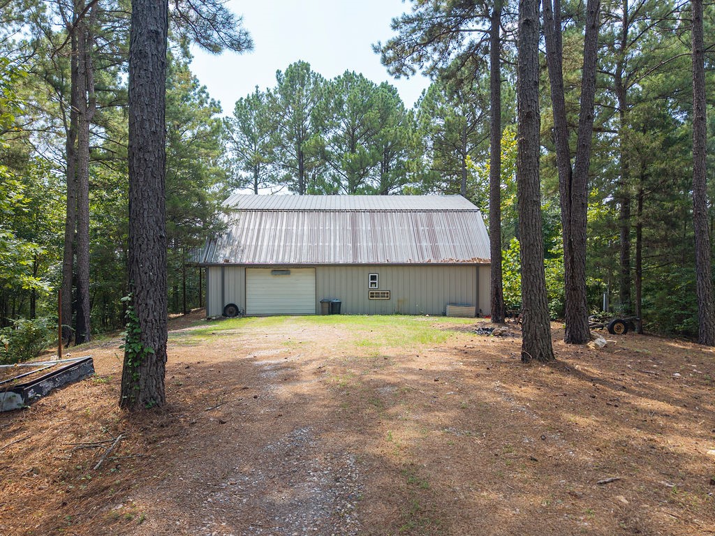 Are you in search of a secluded residence nestled among five acres of majestic pines, with convenient access to Lake Ouachita and recreational activities, all within a 45-minute drive to Hot Springs? This home and shop may be the perfect fit. The shop encompasses approximately 2,500 sq ft, with second-level living quarters offering 1,500 +/- sq ft of open-concept space. Freshly painted in grey, it includes an eat-in kitchen, three bedrooms, two and a half bathrooms, and a utility room. The shop provides ample space for vehicles, SUVs, and boats, plus a heated and cooled office with a half bath. Wired with 220-volt power and well lit, it’s ideal for projects, recreation, or other pursuits. With five acres, the property also allows investment opportunities such as rental storage or short/long-term stays. A small, year-round creek runs along the southern edge, enhancing its charm. With Lake Ouachita, fishing, and hiking trails nearby, the possibilities are endless.