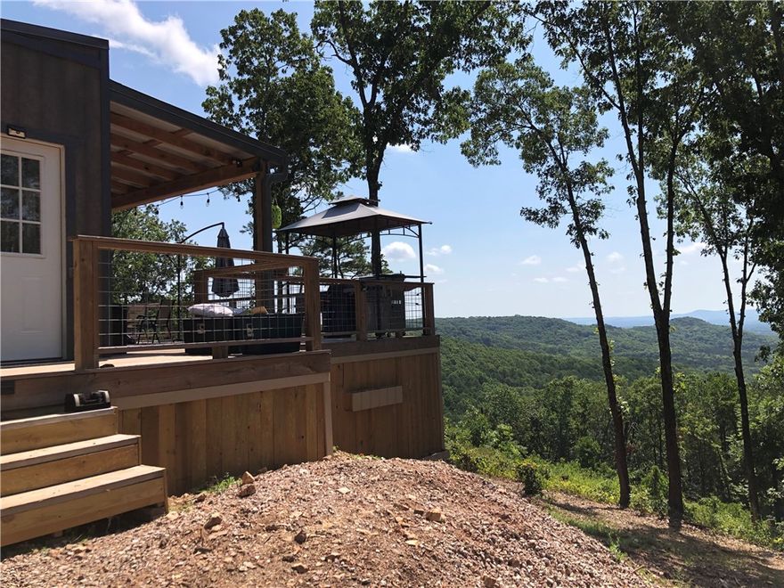 Modern Cabin Retreat with Breathtaking Views on 7.69 Acres! A modern take on the classic cabin—rustic on the outside, sleek and stylish within. The property spans 7.69 acres atop a high ridge line offering expansive sunrise views and peaceful seclusion. A powered gate welcomes you home, while a secondary drive provides leveled parking for trailers, ATVs, and boats. Inside, find a bright clean living space with two bedrooms featuring gorgeous valley views. The kitchen shines with a Samsung high-efficiency refrigerator, Galanz combo oven (microwave, air fryer, and convection), plus KitchenAid electric cooktop and dishwasher. Step outside to 1,000+ sqft of deck space featuring an 8-person Nordic Spa, gas fire pit, grill, smoker, and dry bar—an entertainer’s dream in the heart of nature. Guests will love the dedicated RV parking with 50 AMP service. Wander down the trail to explore the bluff, small cave, and wet-weather creek—or forage for morels, ginseng, and other Ozark treasures. Seeing is believing!