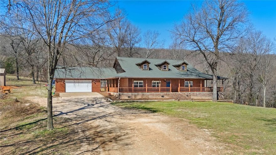 Ozark Mountain retreat on 42 +/- acres just outside Prairie Grove! This 3BR, 2BA home offers approx. 2,200 +/- sq ft of living space with a warm, inviting feel, vaulted ceilings, & abundant natural light. The kitchen features ample cabinetry & workspace, opening to spacious living & dining areas ideal for everyday living or entertaining. The living area includes a wood-burning stove, & the TV conveys. A dedicated office overlooks the wraparound porch w/t scenic views. The large primary suite features a walk-in closet & an oversized bathroom w/t double vanity & tiled dual-head shower. Enjoy the expansive wraparound porch overlooking rolling pasture, two ponds, hardwoods, fruit trees, & berry bushes—perfect for relaxing & taking in wildlife. The land offers endless possibilities for recreation, hunting, or hobby farming. Additional features include a large detached shop/garage w/t 220 amps and private drive. Conveniently located just minutes to Prairie Grove and a short drive to Fayetteville & the U of A.