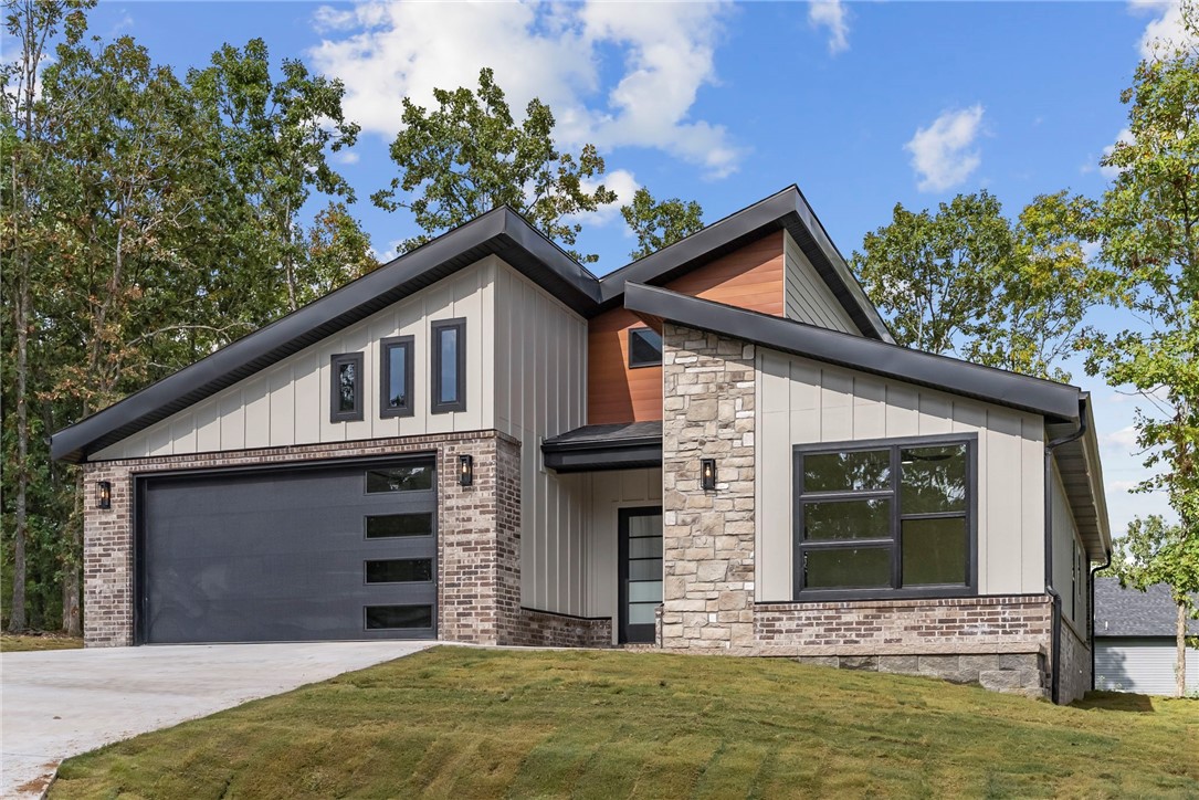 This beautifully crafted modern-style home blends sleek design with natural charm. The striking exterior showcases gorgeous rock accents, durable Hardie board, and warm wood siding for incredible curb appeal. Inside, white oak hardwood flooring flows throughout the main living spaces, while tile highlights the wet areas. Both bathrooms feature upgraded custom tile work, and the spa-like primary suite includes a relaxing soaker tub for the perfect retreat. The open layout creates an easy flow between the kitchen, dining, & living areas, designed for both comfort and entertaining. Step outside to the covered back patio, ideal for enjoying the peaceful setting. The yard offers mature trees for shade and character, balanced with cleared areas for simple maintenance. Just minutes from lake access, this home provides the perfect blend of everyday living and the outdoor lifestyle Bella Vista is known for. With its modern finishes, thoughtful details, and prime location, this new construction is ready to welcome you home.