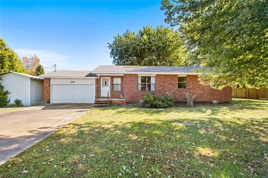 Prime location with endless potential! Discover this fantastic 3 BR, 1.5 BA home situated on a level 0.46-acre +/- lot in the heart of up-and-coming Pea Ridge. City park and schools with easy access. The property features a spacious, flat backyard with mature trees and privacy fencing on two sides. Ample storage and utility space are provided by an attached two-car garage and two exterior outbuildings, including a separate garage structure and a storage shed. The interior layout is practical, featuring all three bedrooms and the full bath conveniently located off a central hall, just off the living room. Entry from the attached garage leads through the utility room with access to the half bath, flowing into the kitchen which opens to a covered and enclosed back deck via a sliding glass door.