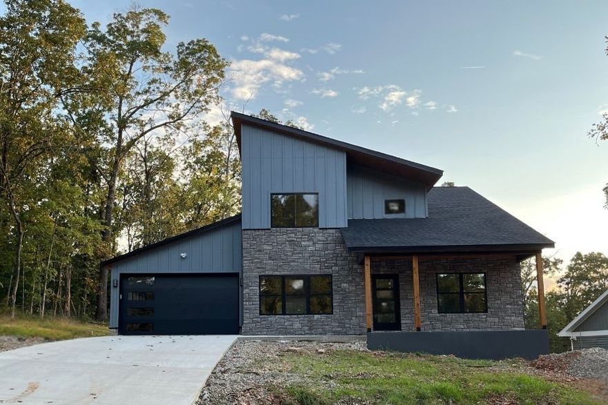 Discover modern living at its finest at 85 Rountree, located within Bella Vista city limits with access to exceptional POA amenities including golf courses, lake access, pools, tennis courts, clubhouses, and trails. This stunning two-story home features an eye-catching exterior with metal & concrete siding, warm wood accents, and stone details, complemented by a two-car garage. The open-concept main level showcases beautiful wood detailing throughout the kitchen, quartz countertops, and striking electric range with gorgeous vent hood. Glass doors open to your private backyard and future upper deck with cable railing. The primary bedroom suite offers a spa-like bathroom with double vanities, walk-in shower featuring marble accent tile, and generous walk-in closet. Upstairs, you'll find a second living area with soaring ceilings, two additional bedrooms, full bathroom with walk-in shower, and abundant storage. With warm wood tones throughout, this home creates perfect atmosphere for comfortable modern living.