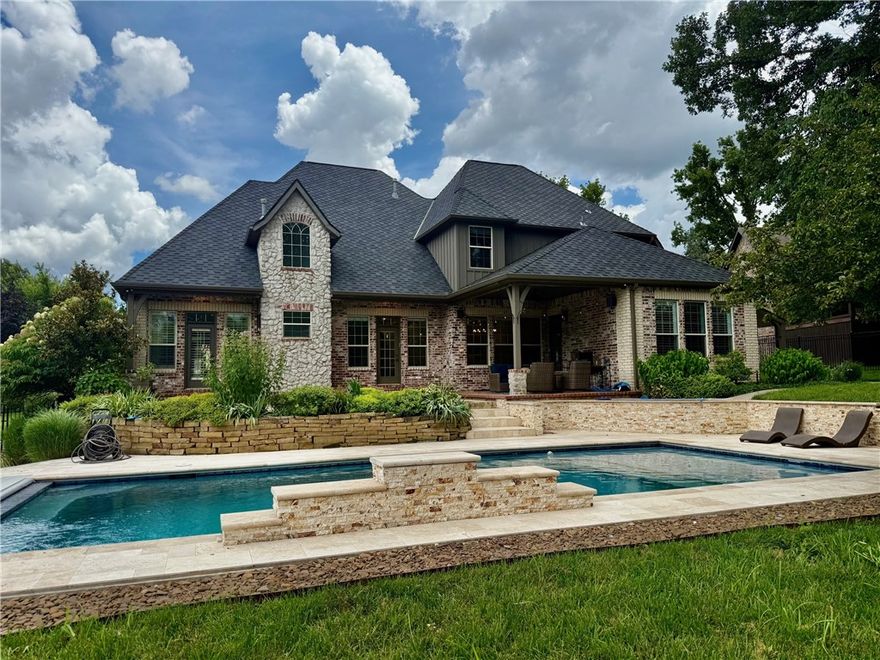 Exceptional estate in Bentonville’s Avignon Subdivision! Situated on over half an acre, this beautifully remodeled home offers architectural stonework, wood flooring, and a floorplan ideal for daily living and entertaining. Grand entry with brick archways, wrought iron staircase, and crisp trim detail. Two main-level bedrooms including a spacious primary suite. Gourmet kitchen features quartz counters, waterfall island, sleek cabinetry, dual wine fridge, hidden refrigerator/freezer, and gas range. Den with custom built-ins and tile-surround fireplace. Dining area accented by exposed brick and beams. Upstairs offers two bedrooms with Jack & Jill bath, family room, and bonus space. Additional features: walk-in pantry, plantation shutters, tankless water heater, 3 HVACs, central vac, and 3-car garage. Enjoy the private backyard with a covered patio, gas grill hookup, lush landscaping, and a beautiful HUGE saltwater pool—all just minutes from downtown, trails, and Crystal Bridges.