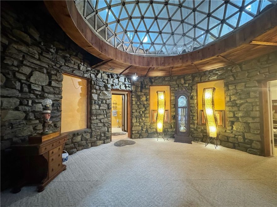 Anything but ordinary! Tucked into the hillside on Pine Hill Rd, on 1.63 acres of land, this circular concrete home offers nearly 2,000 sq ft of fully finished, livable space on the main level, anchored by a striking rock room with an atrium above that once filled the space with natural light. Imagine a stunning spiral staircase leading to the second level, where over 3,000 sq ft is already framed, wired, roofed, windowed, and partially plumbed, ready for your design to take over. With the right vision, this could be a true architectural statement. Downstairs would be great for a multi-generational suite, offering the peace of mind of having your loved under the same roof while enjoying your own privacy on the second floor. Exterior stonework could be tied in beautifully to bring it all together. There’s also a two-car garage, plus a massive attached shop with oversized doors tall enough for an RV and a half bath, perfect for projects or storage. This is a rare chance to create something unforgettable! SOLD AS IS.