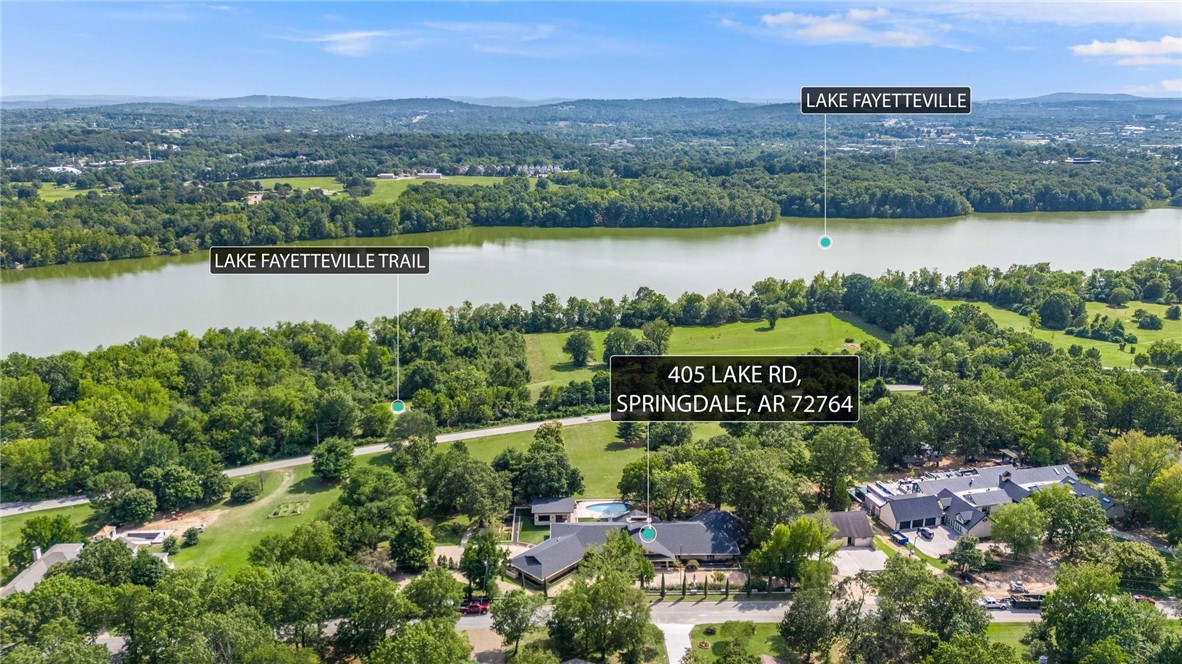 Iconic Mid-Century Estate with Lake Fayetteville Views–A Springdale Legacy. Step into a piece of Springdale history with this architecturally significant home, originally built in 1950 by renowned local builder and city icon Sandy Boone for Joe and Gretchen Steele. Perched on 4.41 acres with unparalleled view of Lake Fayetteville, this one-of-a-kind property offers nearly 7,000 sq ft of beautifully designed living space, including a 2,500 sq ft separate gym. Constructed with rare fossilized limestone block, the home's timeless mid-century design is enhanced by recent, high-end updates. The primary suite, completely remodeled in 2025, features dual spa-like bathrooms, refined finishes, and a serene, private retreat with modern elegance. Seven expansive sliding glass doors line the back of the home, seamlessly blending indoor and outdoor living while providing panoramic views of the newly resurfaced pool, cabana with outdoor kitchen, and the surrounding natural landscape—a true gem in Springdale’s real estate market.