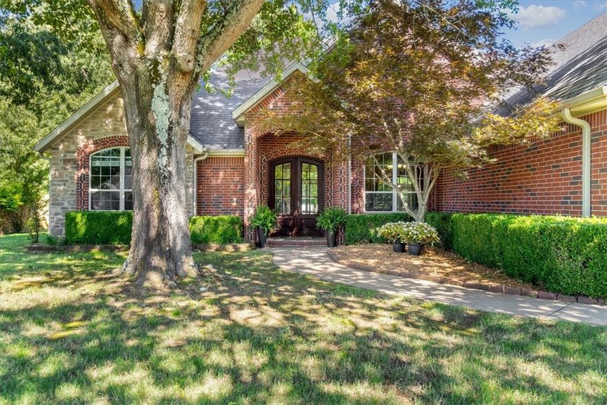 This masterfully built 3117 sq/ft. 4-bedroom custom home on the west side of Fayetteville features a 2.75-acre wooded lot, 3 car garage and 3 full bathrooms. Ample shade is provided by mature trees with a beautiful brick and stone elevation. Double front doors open to beautiful hardwood flooring and full home crown molding. Natural light fills the great room through the oversized windows shining light onto the wood stove insert which hides a gas hookup.
Cooking is a snap accessing your food from the dual pantries utilizing your gas cooktop and double oven while the granite topped island offers both storage and seating. The back porch is a perfect space to sit or dine and enjoy a secluded, wooded view featuring prime bird and wildlife viewing. The primary bedroom’s generous size can host a large bedroom suite with room to spare featuring a trayed ceiling and an ensuite with two vanities, jetted tub, walk-in double headed shower and a walk through closet.