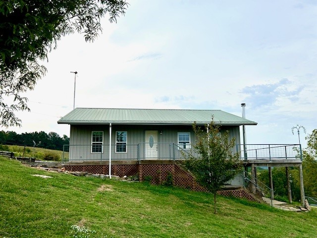 3-bedroom, 2-bathroom situated on 54.5 acres, offering exceptional views. The kitchen is designed with windows that showcase the scenic surroundings. Beautiful hardwood flooring on the main level. The home features a wraparound deck and has been designed to be fully accessible for individuals with disabilities. It is equipped with a professionally installed wheelchair elevator, ramps, handrails, and wide doorways that accommodate wheelchair access. Additionally, the walkout basement includes a storm shelter for enhanced safety, and a wood-burning stove is present in the living area. The property is entirely fenced and includes a hunting cabin, chicken coop, work shed, attached garage, detached carport, three ponds, one of which is spring-fed and includes a spring house. The land consists of 20.5 acres designated for pasture and 35 acres of wooded terrain.