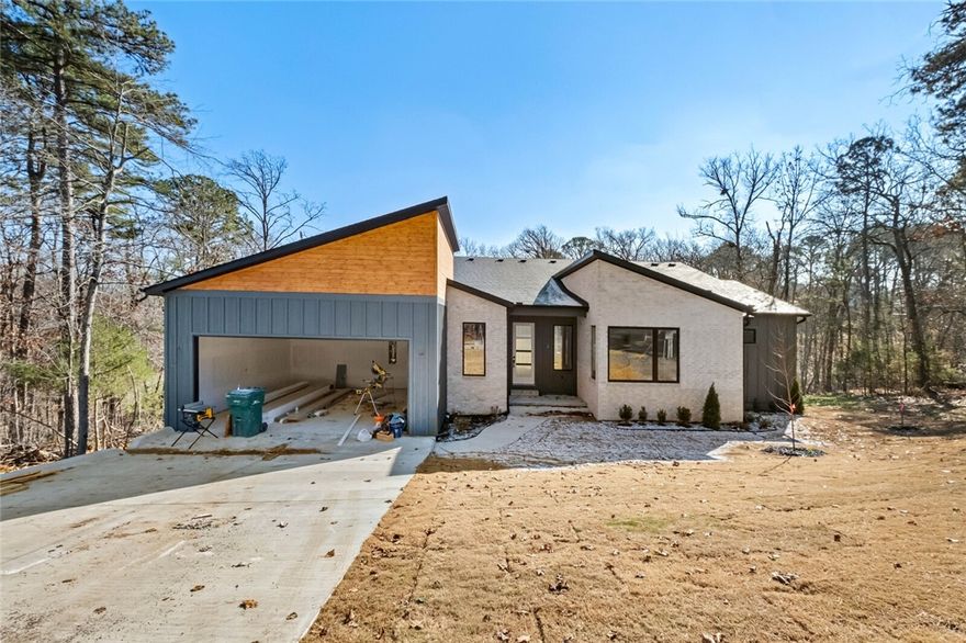 Modern design meets wooded serenity in this stunning new-construction home! Clean lines, designer exterior finishes, and expansive windows create a bright, contemporary feel throughout. Enjoy seamless indoor–outdoor living with a huge covered deck and a spacious lower patio overlooking the trees. The sleek entry, open layout, and elevated architectural details make this home truly one-of-a-kind. A rare find offering privacy, style, and quality craftsmanship in a peaceful Bella Vista setting. Builder is offering a 1-year warranty.