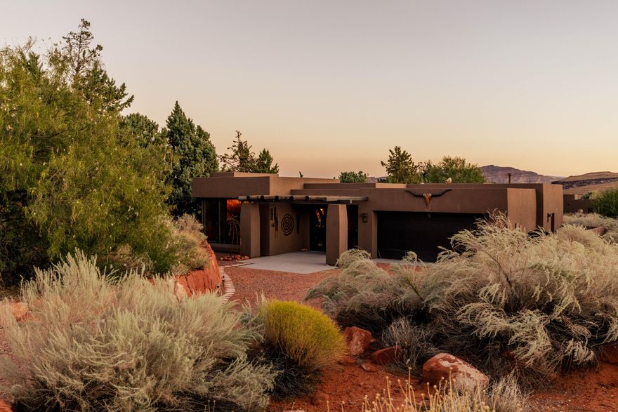 Welcome to a stunning single-level custom home at the base of the iconic Kayenta red rock mountains in Ivins. This 2,404 sq ft residence showcases exceptional craftsmanship and Southwest elegance with hand-finished log ceilings, a dramatic red rock accent wall, and custom niches with art lighting. The gourmet kitchen impresses with two-tone cabinetry, stainless steel appliances, and a 9-ft hand-carved island with custom resin inlay. Two oversized master suites feature spa-inspired baths, walk-in closets, and individual climate control. A spacious sunroom with retractable glass doors opens to a private backyard with gazebo, stucco privacy wall, and beautifully maintained low-maintenance landscaping. Experience the beauty of Kayenta living- schedule your showing today.