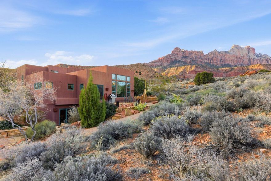 This modern custom Zion home is situated high in the foothills adjacent to Zion National Park Lands. The full glass windows showcase the beautiful native scenery complete with full views of the iconic red rocks of Zion on both sides of Zion Canyon. The open concept floor plan lends itself both to small intimate gatherings yet easily handles large crowds. From the entry doorway, you look directly on to an amazing limestone patio with terraced water feature. The kitchen is partially enclosed, yet flows seamlessly into the Dining Room and Great Room. Patios off the Dining Room and the attached Mother-in-law area allow for year round outdoor living. The primary bedroom is perched where the views are expansive and unobstructed. Two additional bedrooms are on the main floor. The MIL suite, and a commercial style kitchen and a large workshop/studio room and plenty of storage are on the ground floor with a ground floor entry. Power bills are minimal with the 30 70KW solar panels. Enjoy the solitude and the natural beauty of Zion where you are away from any crowds, and have your own private retreat.