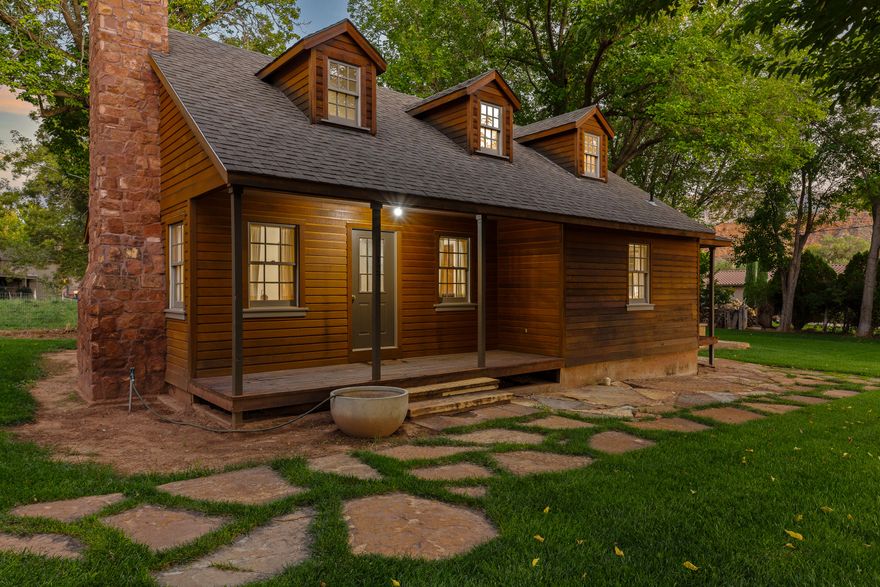 Step back in time and discover the heartwarming embrace of this authentically restored 1944 Rockville cottage. Steeped in history, this home weaves a story of timeless charm and quiet comfort. The moment you enter, you're greeted by the rich glow of original wood flooring, whispering tales of decades past. The darling living room, anchored by a classic brick fireplace, invites you to gather and create new memories.
The spacious kitchen and dining area feel like the heart of the home, ready for warm meals and lively conversation. Follow the home's gentle history upstairs to a finished attic, a storybook space, perfect for visiting guests or a quiet retreat.
The magic continues outside, where a wrap-around porch overlooks a private sanctuary. Nestled under a canopy of mature shade trees, you'll find hand-hewn stone benches for quiet contemplation and a unique all-stone soaking pool, offering a tranquil escape with views of the majestic red rock landscape. Located on Rockville's historic Main Street, this cottage isn't just a home; it's a piece of history, offering a peaceful life near the grandeur of Zion National Park.