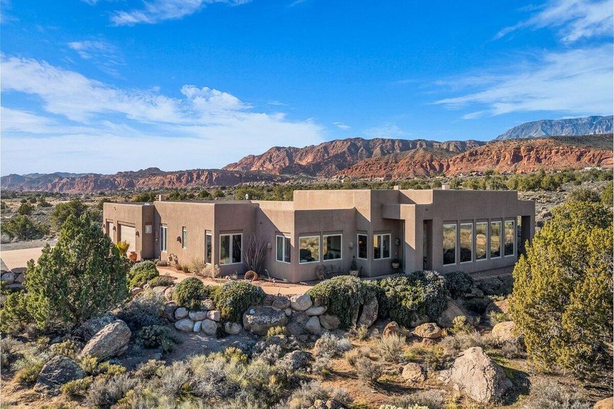 Perched on a generous 1.23-acre lot, this exceptional home showcases breathtaking 360-degree views of the Pine Valley and Zion Mountains, offering peaceful morning sunrises from the kitchen window and stunning evening sunsets from the living room and primary bedroom. Soaring 12-13 foot ceilings and windows on all sides flood the home with natural light and create an open, airy atmosphere throughout. The inviting living and dining spaces are warmed by two elegant gas fireplaces, adding both charm and comfort for everyday living or entertaining guests. The chef's kitchen is a true centerpiece, featuring dual oversized islands, one finished with thick granite and the other with a beautiful butcher block, along with two pantries for abundant storage and functionality. The serene primary suite offers a unique walk-in hallway with floating shelves and bookshelves, leading to a spa-like bathroom with direct walk-out access to the back patio. Step outside to the expansive patio with pergola, perfectly designed for outdoor living with a built-in BBQ sink, ceiling fans, and speaker wiring, making it ideal for hosting or relaxing while taking in the views. Completing the home are a spacious laundry/craft room, a brand-new 2025 water heater, a massive 3.5-car garage with extra depth for golf carts, and plenty of room on the lot to build a future casita or additional amenities. Buyer to verify all information, deemed reliable, however buyer to verify all info including utilities, rental restrictions, and HOA information if applicable.