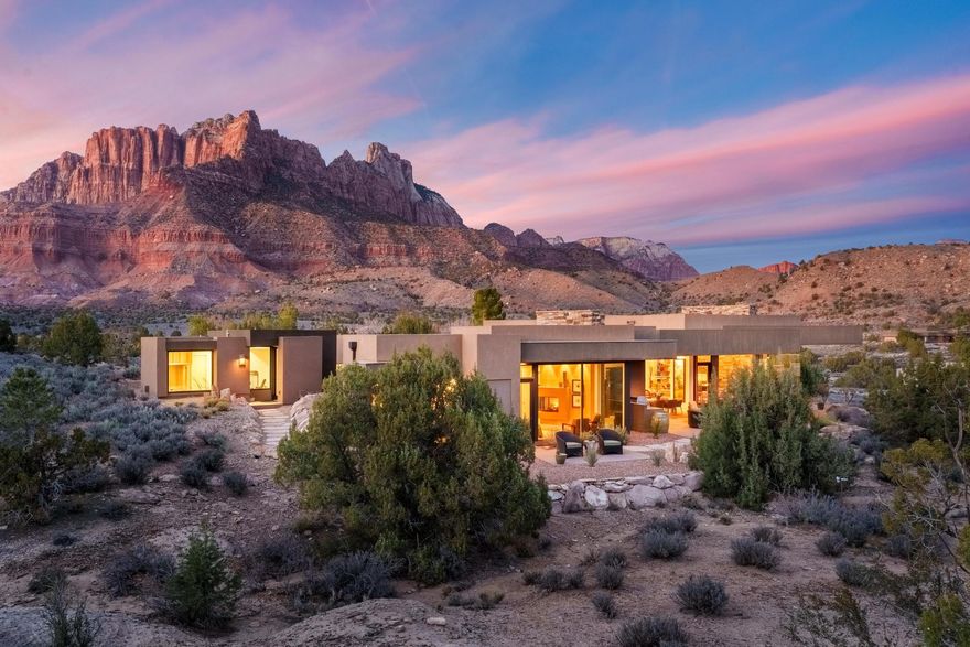Where the Desert Whispers and the Mountains Stand Guard

At the gates of Zion National Park, this extraordinary 3,970 SF custom home rests on .39 acres on the Anasazi Plateau, surrounded by conservation easements and breathtaking 360° mountain views. Built in 2016 and designed by acclaimed architect Rob McQuay, the residence blends modern architecture with the raw beauty of Southern Utah.

A sculptural, ADA-accessible front door sets the tone, complemented by hand-selected stone from the Hurricane rock quarry. Inside, soaring wood doors, polished concrete floors, and walls of glass create gallery-like calm. Retractable dining room doors disappear into the wall for seamless indoor-outdoor living framed by Zion's glowing cliffs.

The chef's kitchen features granite and quartz countertops, walk-in pantry, dedicated coffee bar, and abundant storage. Premium appliances include Bosch double ovens, cooktop, hood and microwave, Thermador refrigerator, and Frigidaire beverage refrigerator--ideal for entertaining after a day in the park.

The primary suite offers a propane fireplace, spa-inspired bath, and generous custom closet with integrated safe. Thoughtful infrastructure includes three-zone A/C, new hard-wired shades, dual grinder pump systems, reverse osmosis system, and whole-house propane generator.

Outdoor living shines with a propane fireplace and custom BBQ with wood, charcoal, and propane capability. The oversized 1,022 SF three-car garage features epoxy floors, built-in storage, and boot wash station.

A detached 498 SF guest house, also designed by Rob McQuay (built 2024), offers concrete floors, fiber internet, two mini-splits, on-demand hot water, sauna, soaking tub, and plumbing for a future kitchen. Separate water meter and grinder pump system.

Design-forward furnishings, including Italian leather pieces curated by Ashley Johnson, may be negotiable.

A rare modern sanctuary at Zion's edge--where architecture and landscape become one.