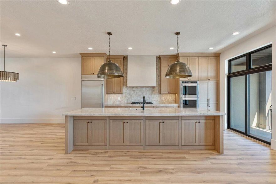 Welcome to this stunning luxury townhome that masterfully blends elegance and functionality all in one! Featuring an open-concept floor plan, this home boasts a spacious kitchen outfitted with custom cabinetry, a large center island with Quartzite countertops, designer pendant lighting, and high-end stainless steel appliances including a gas cooktop and double wall ovens. The rich wood tones and soft neutral finishes create a warm, timeless aesthetic. Enjoy indoor-outdoor perfect for entertaining. The main living area is adorned with wide-plank luxury flooring, custom lighting, and recessed ceiling fixtures to highlight the home's modern charm.