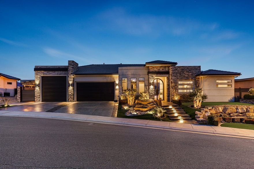 This exquisite luxury residence seamlessly blends contemporary elegance with modern sophistication. Situated above the renowned Sunbrook Golf Course, it offers breathtaking, unobstructed panoramic views of red rock formations, desert landscapes, and majestic mountain horizons. Enter through grand double iron-and-glass doors, accented by designer lighting, into a bright, open main living area. A dramatic 10' × 20' disappearing glass wall glides into its hidden pocket, effortlessly merging the great room with the resort-style backyard—creating a true open-air pavilion experience. The chef's gourmet kitchen features premium Café appliances and sleek quartz countertops, perfect for everyday living and entertaining. The indulgent primary suite includes a meticulously designed walk-in closet with custom jewelry cabinetry, drawers, shelving, and racks, plus a spa-inspired bath with a separate garden tub, full-height glass shower with elegant tile-work, and motorized blinds throughout the bedrooms and primary bath. Key refinements include an oversized custom barn door, ceiling fans in all bedrooms, large-scale fans in the family room and patio, and a whole-home water softening system. The entertainer's backyard is a private oasis: custom pool with integrated jetted hot tub, dual fire pits, underwater illumination, sheer-descent waterfall, and unique metal palm tree accents. Mediterranean-inspired planters feature boxwoods, iceberg roses, palms, and hundreds of complementary plants. Low-maintenance artificial turf covers the front, back, and sides, complete with a private 3-hole putting green. Enjoy year-round outdoor living under a powered retractable awning and metal patio cover on one side, with a golf cart carport and fully enclosed custom dog run on the other. The fully fenced grounds include steel and composite gates and fencing, plus a full-height block wall for privacy and security. The oversized garage is a gear enthusiast's dream, featuring epoxy floors, RV/boat parking capability, a full wall of New Age Pro Series lockers, toolboxes, heavy-duty racks, a 4-post car lift, and mini-split AC/heating. Additional enhancements include a custom front-yard water feature, level-tiered front yard with raised planters and seating, custom concrete steps and sidewalk with integrated step lighting, and premium concrete finishes on the driveway, patios, and side yards. More than a home, this is a private desert sanctuary where sophisticated design meets effortless luxury living framed by championship golf and iconic Southern Utah vistas. Welcome to elevated modern elegance.
