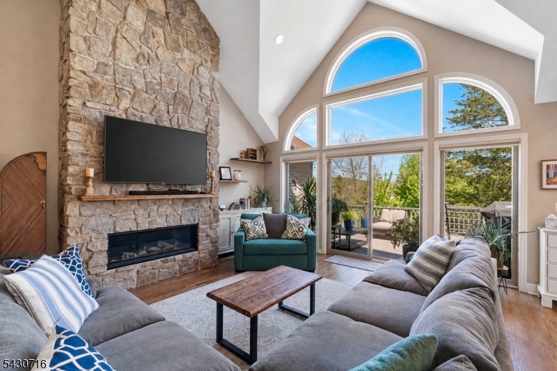 Living room with a stone fireplace, vaulted ceiling, and large arched windows overlooking trees.