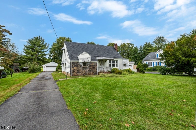 White single-story house with a stone facade, broad lawn, and driveway leading to a detached garage.