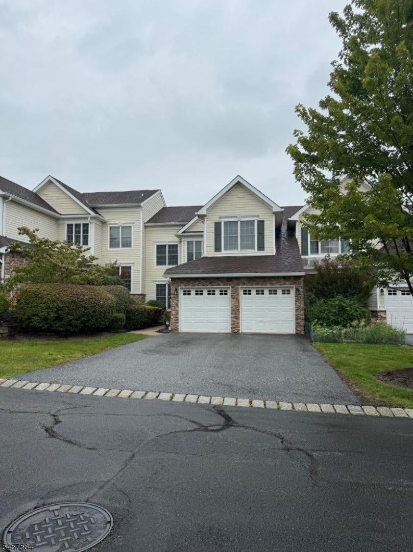 Attached home with pale siding, stone accents, and a two-car garage facing a wide paved driveway.
