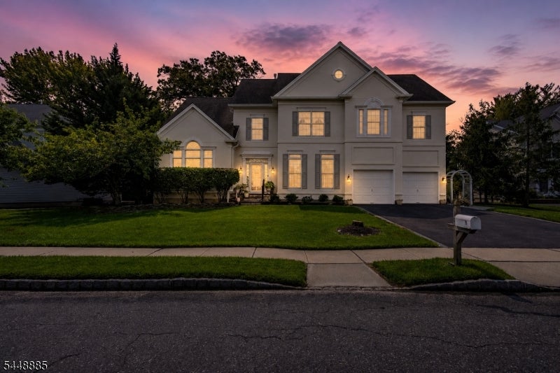 Two-story home with glowing windows, an attached garage, and a front lawn at dusk.