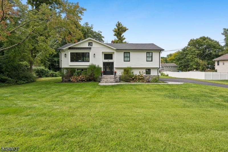 Light-colored split-level home with front steps and a broad lawn beneath mature trees.
