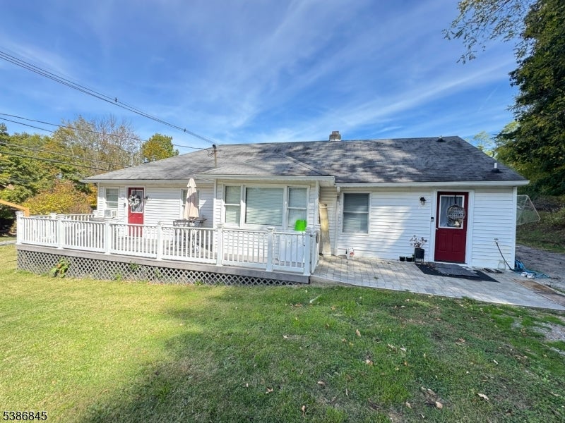 Single-story white house with red doors, a raised deck, paved patio, and broad lawn.