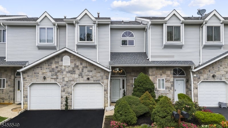 Attached townhouses with stone facades, white garage doors, and landscaped shrubs.