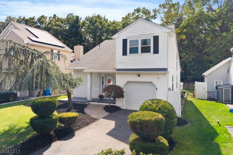 White two-story house with an attached garage, curved front walkway, and neatly trimmed shrubs.