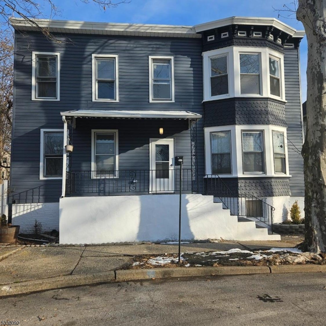 Two-story dark-sided house with a white-trimmed bay window and covered front porch.