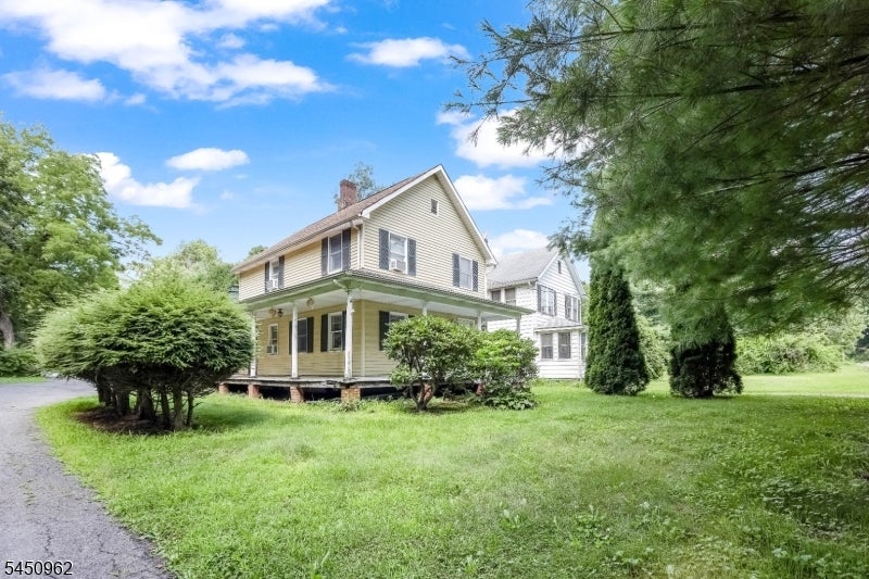 Two-story yellow house with a covered porch, broad lawn, and mature trees.
